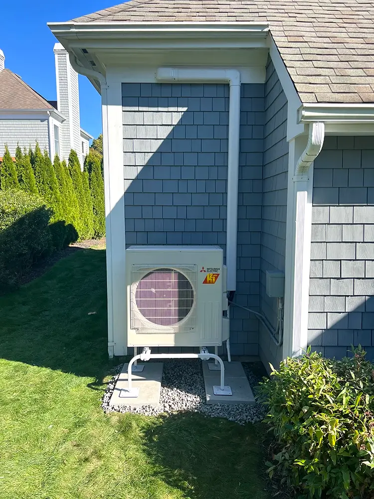 Exterior Mitsubishi ductless condenser and piping installed on the side of a house in Cumberland, RI by National Refrigeration